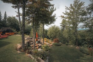 A landscaped garden with a wooden deck, picnic tables, and a stone pathway. - Luxury log cabin 1 hour from Montreal (Mille-Isles)