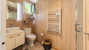 Un baño moderno con pared de madera, un lavamanos blanco, un inodoro, un perchero para toallas y una zona de ducha.