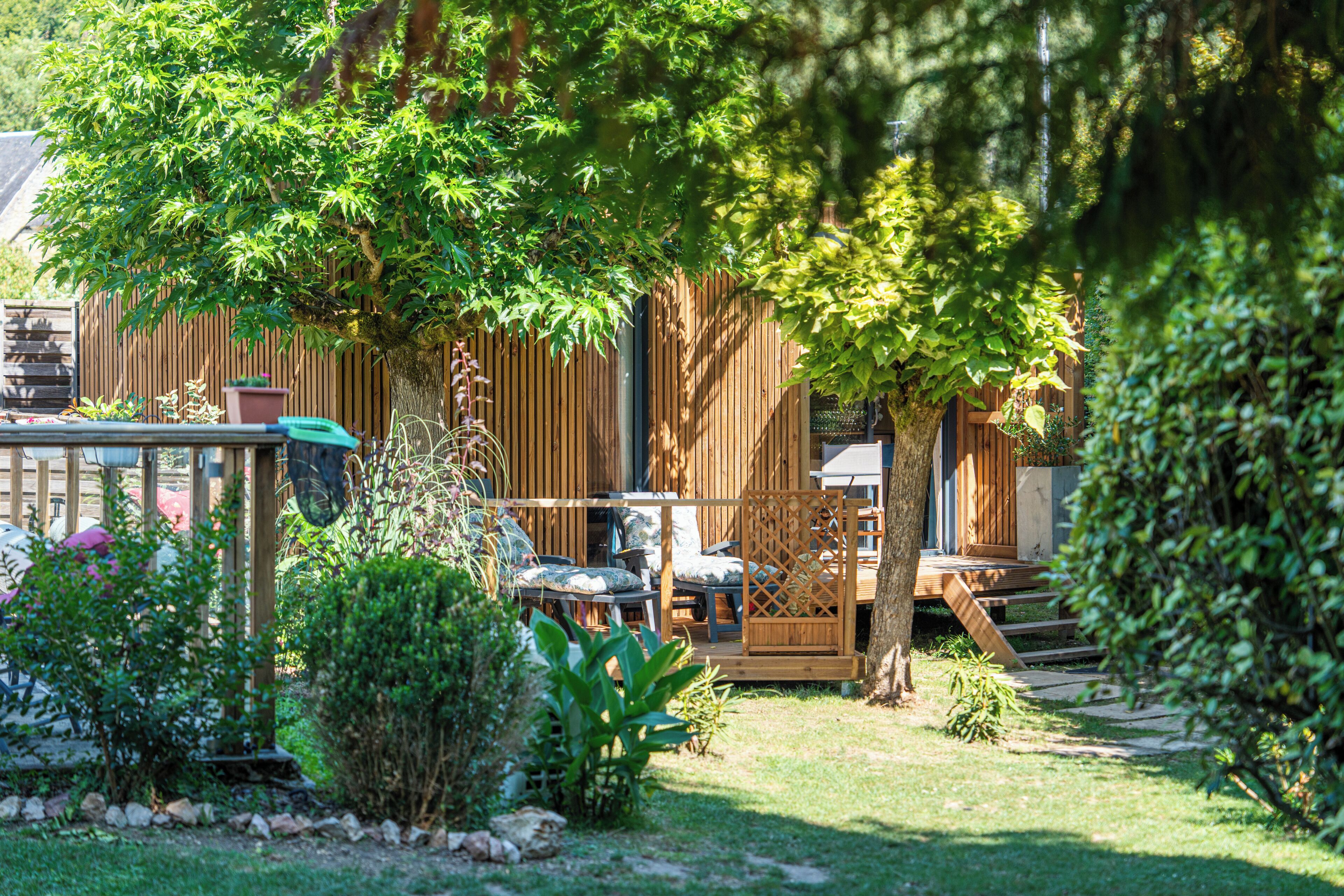 Una terraza de madera con mobiliario exterior, rodeada de exuberante vegetación y una valla de madera.