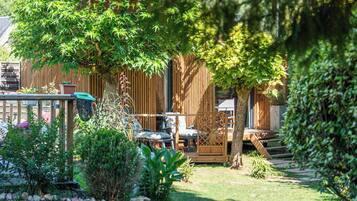 Una terraza de madera con mobiliario exterior, rodeada de exuberante vegetación y una valla de madera.