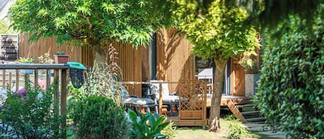 Une terrasse en bois, agréée de mobilier d’extérieur, entourée d’une végétation luxuriante et d’une clôture en bois.