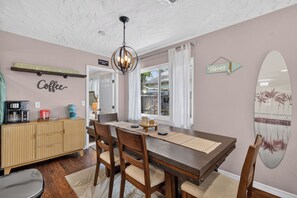 A dining area with a wooden table, chairs, a coffee station, and a view of the outdoors through a window.