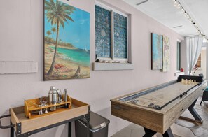 A pool table with a wooden finish and metal accents, a bar area with a tray of bar tools, and a wall with tropical-themed paintings. - Kylia Kove Family Retreat Minutes From Anna Maria Island (Bradenton)