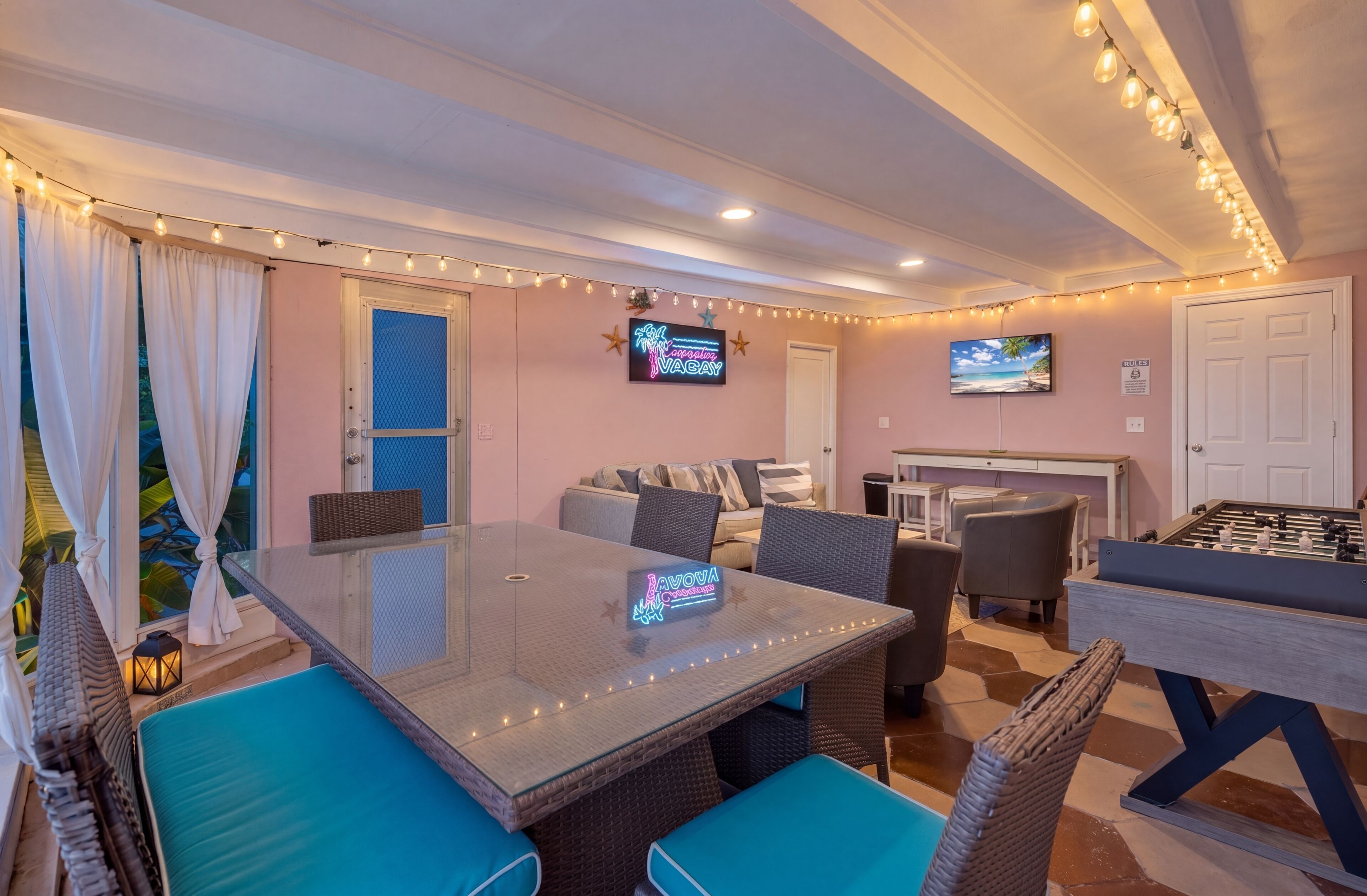A room with a glass-top table, wicker chairs, a sofa, and a foosball table.