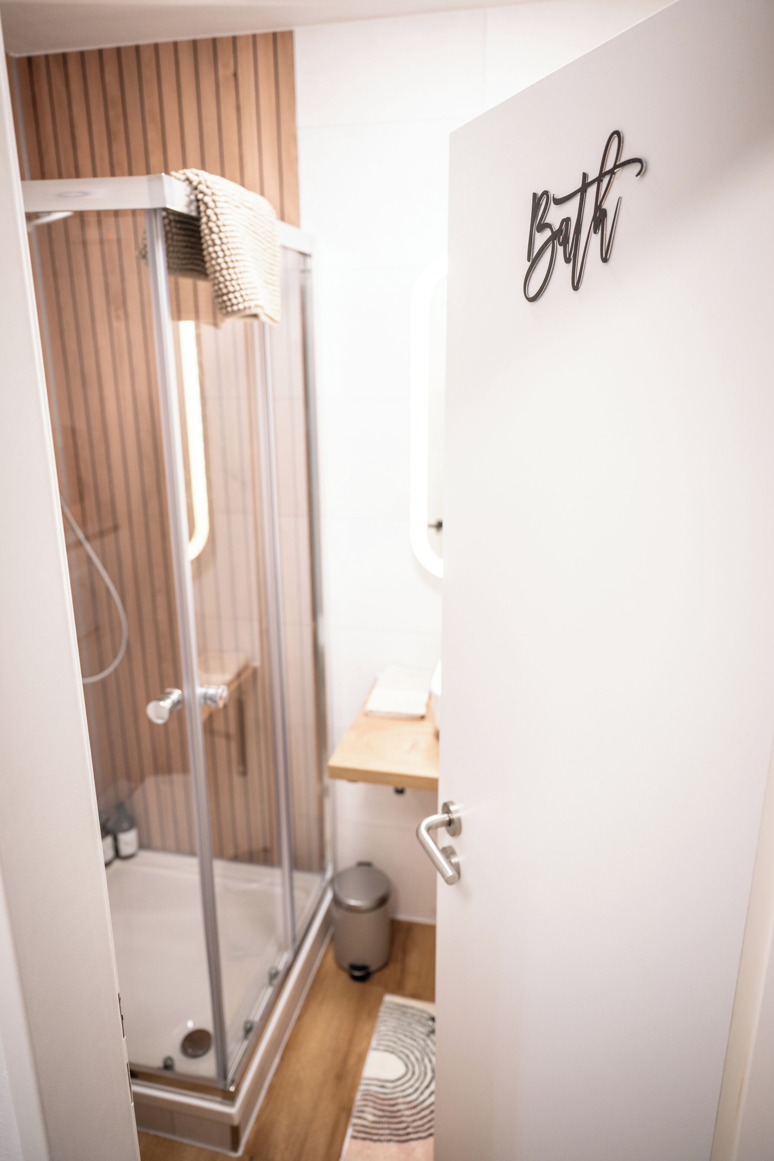 Ein modernes Badezimmer mit einer Duschkabine aus Glas, einer Wand mit Holzlatten und einem Schild mit der Aufschrift 'Bad' an der Tür.