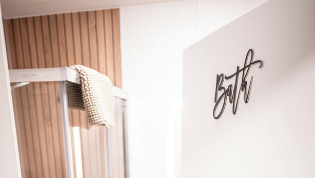 A modern bathroom with a glass shower enclosure, a wooden slatted wall, and a 'bath' sign on the door. - Charming 1-bedroom riad in the heart of Freiburg im Breisgau (Freiburg im Breisgau)