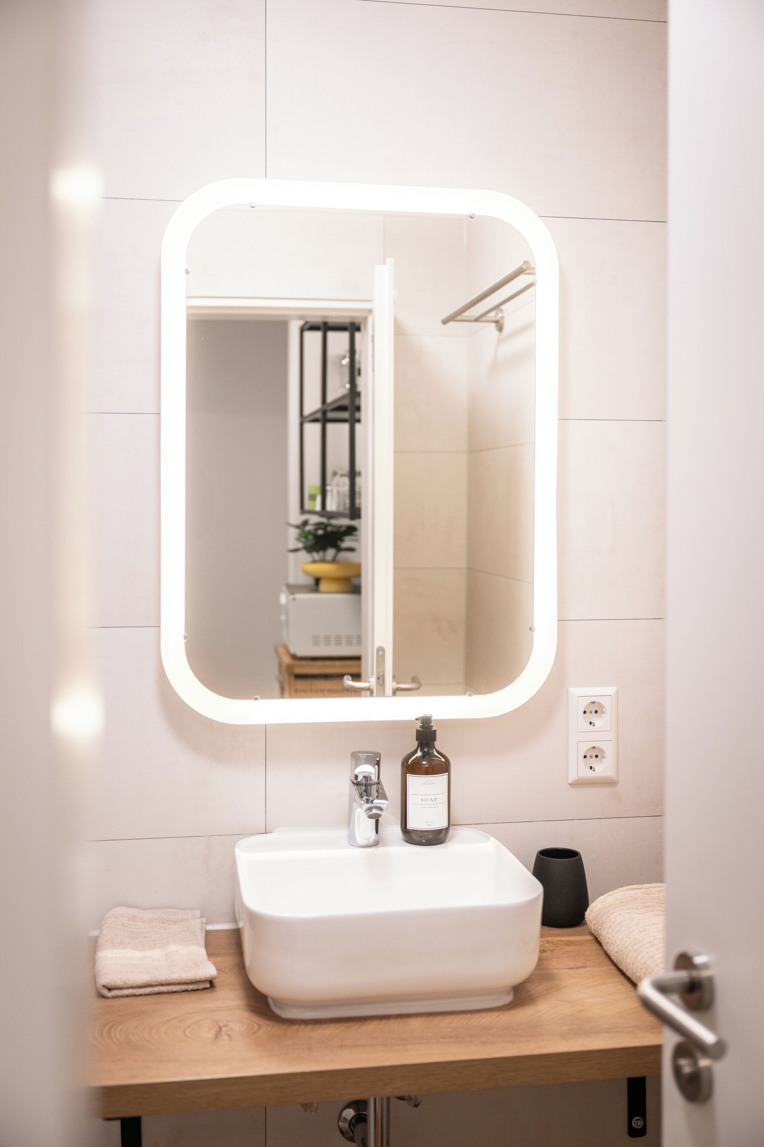 Ein Badezimmer mit weißem Waschbecken, einem Spiegel mit Beleuchtung und einem Handtuch auf der Ablagefläche.