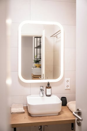 Un bagno con un lavandino bianco, uno specchio illuminato e un asciugamano sul ripiano.