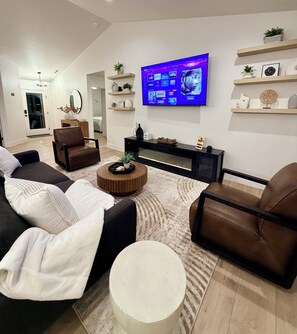Un salon moderne doté d’un téléviseur à écran plat fixé au mur, d’une cheminée et d’un espace détente avec des canapés et une table basse.