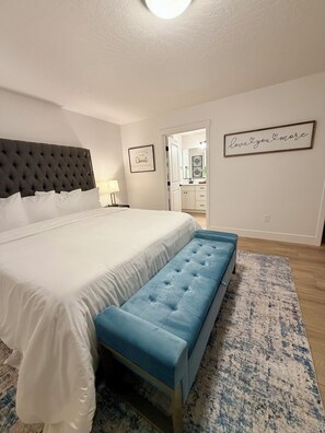 Ein Schlafzimmer mit einem großen Bett, einer blauen Bank, einem weißen Kopfteil und einer Wand mit einem gerahmten Motivationszitat.