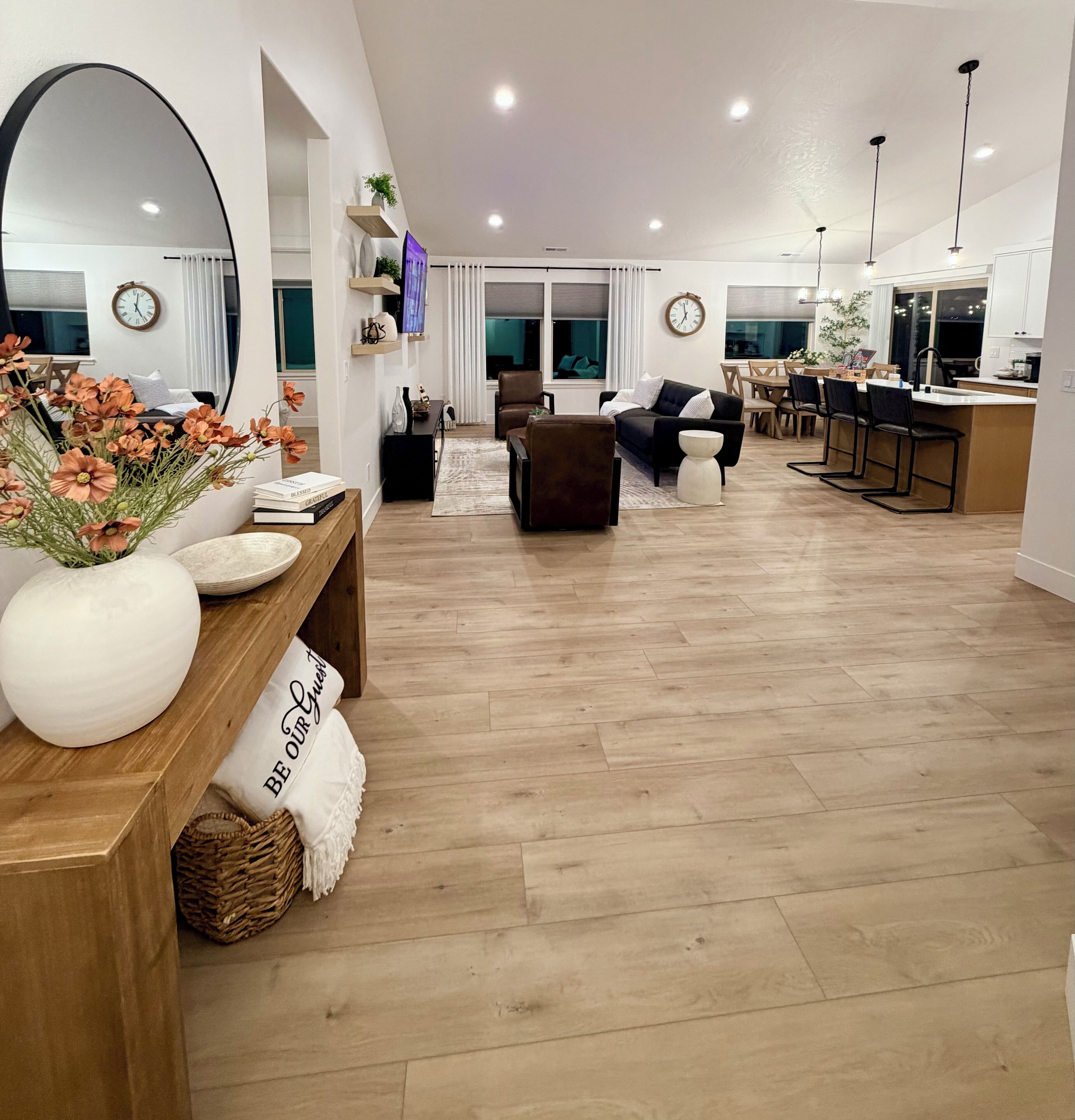 Un vaste espace de vie doté d’un plancher en bois, d’un grand miroir, d’un canapé, d’une table basse et d’un coin repas avec des chaises et une table.