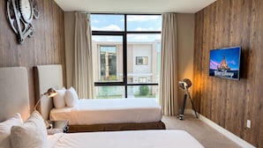 Ein Hotelzimmer mit zwei Betten, einem an der Wand befestigten Fernseher und einem großen Fenster mit Blick auf Gebäude.