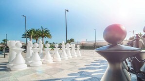 A series of white, uniquely shaped tables arranged outdoors on a tiled floor, with palm trees and a clear sky in the background. - Magic Village Paradise 4BR (Kissimmee)