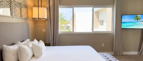 A hotel room with a large bed, a television, and a window with a view of buildings and palm trees.