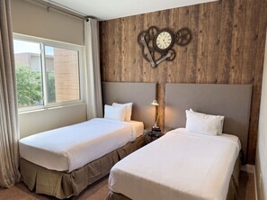 Habitación de hotel con dos camas, una pared de madera con un reloj y una ventana con cortinas.