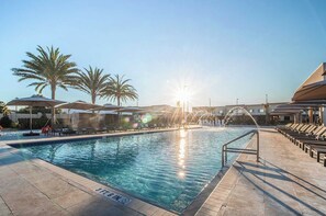 A pool area with sunlit water, palm trees, and lounge chairs.