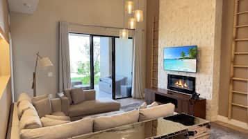 A modern living room with a sofa, a glass coffee table, a fireplace, and a TV mounted on a brick wall.