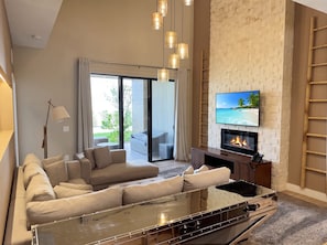 A modern living room with a sofa, a glass coffee table, a fireplace, and a TV mounted on a brick wall. - Magic Village Paradise 4BR (Kissimmee)