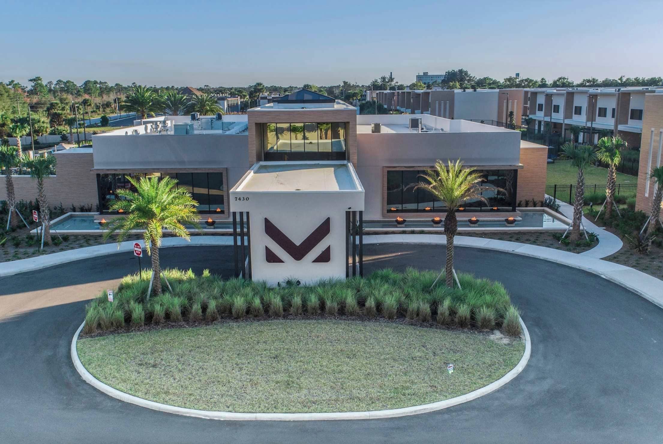 A modern building with a large entrance, a parking area, and a landscaped garden with palm trees.