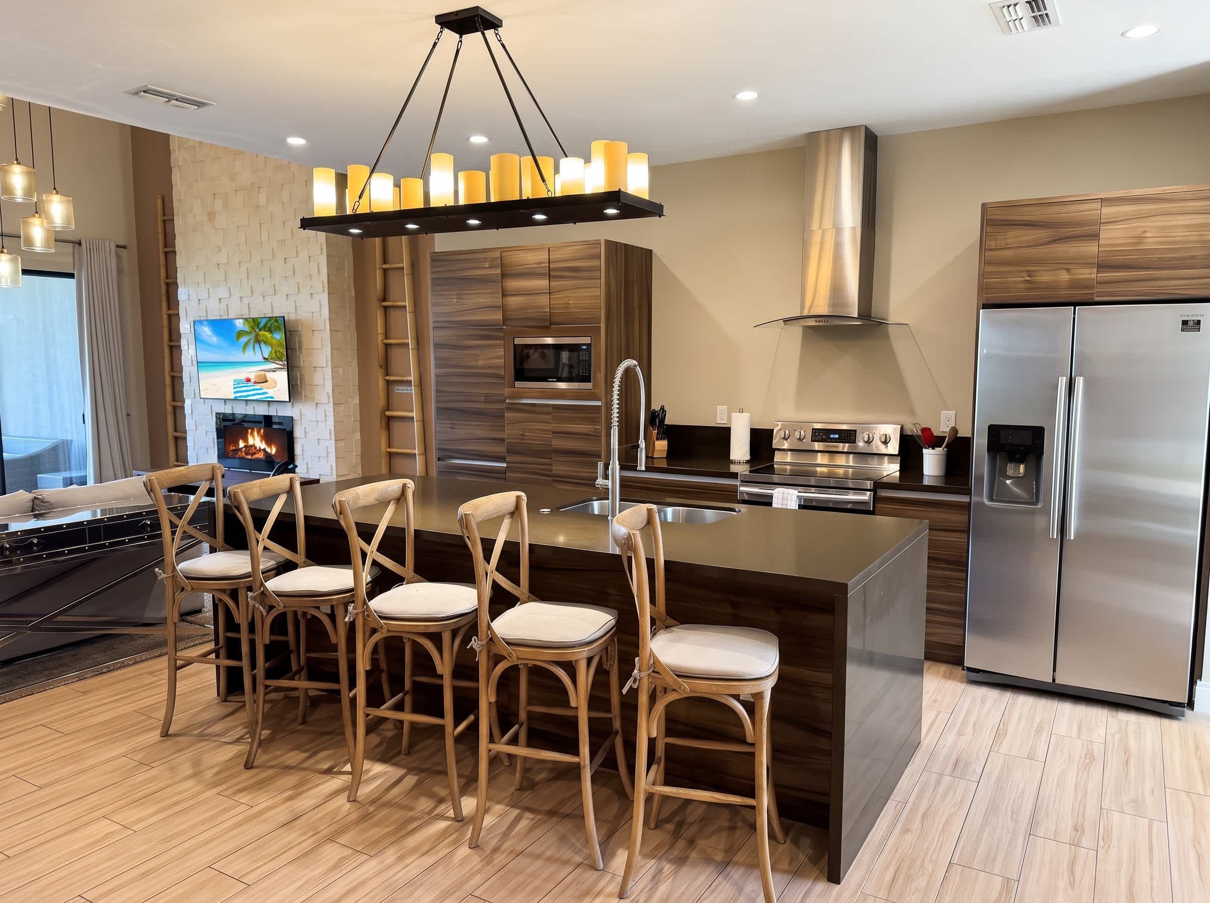 A modern kitchen with a central island, stainless steel appliances, and a seating area with wooden chairs.