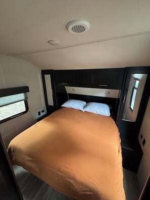 A compact bed with a headboard, a window, and a ceiling vent.