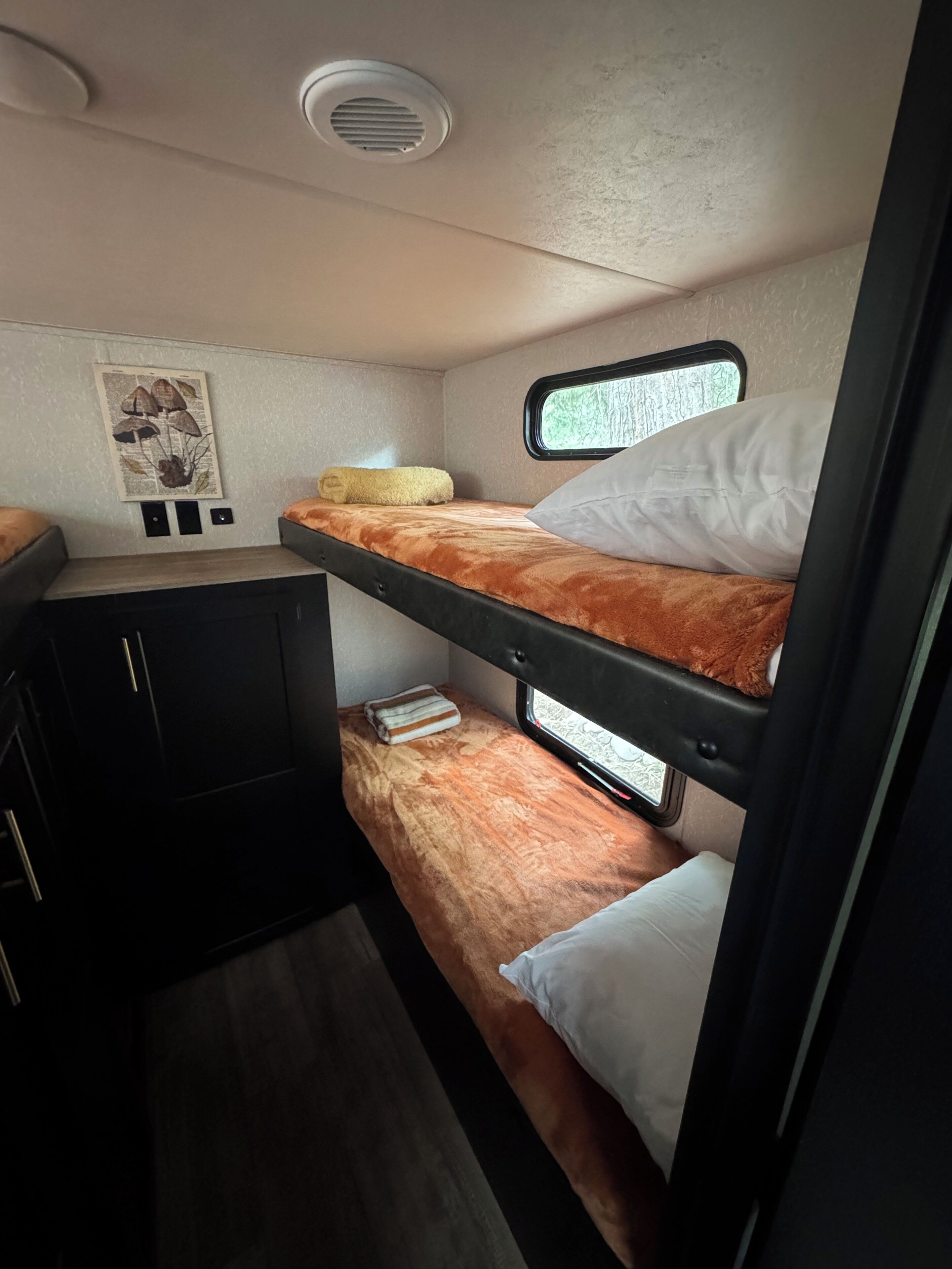 A compact RV interior with a bunk bed, a small kitchenette, and a window providing a view.
