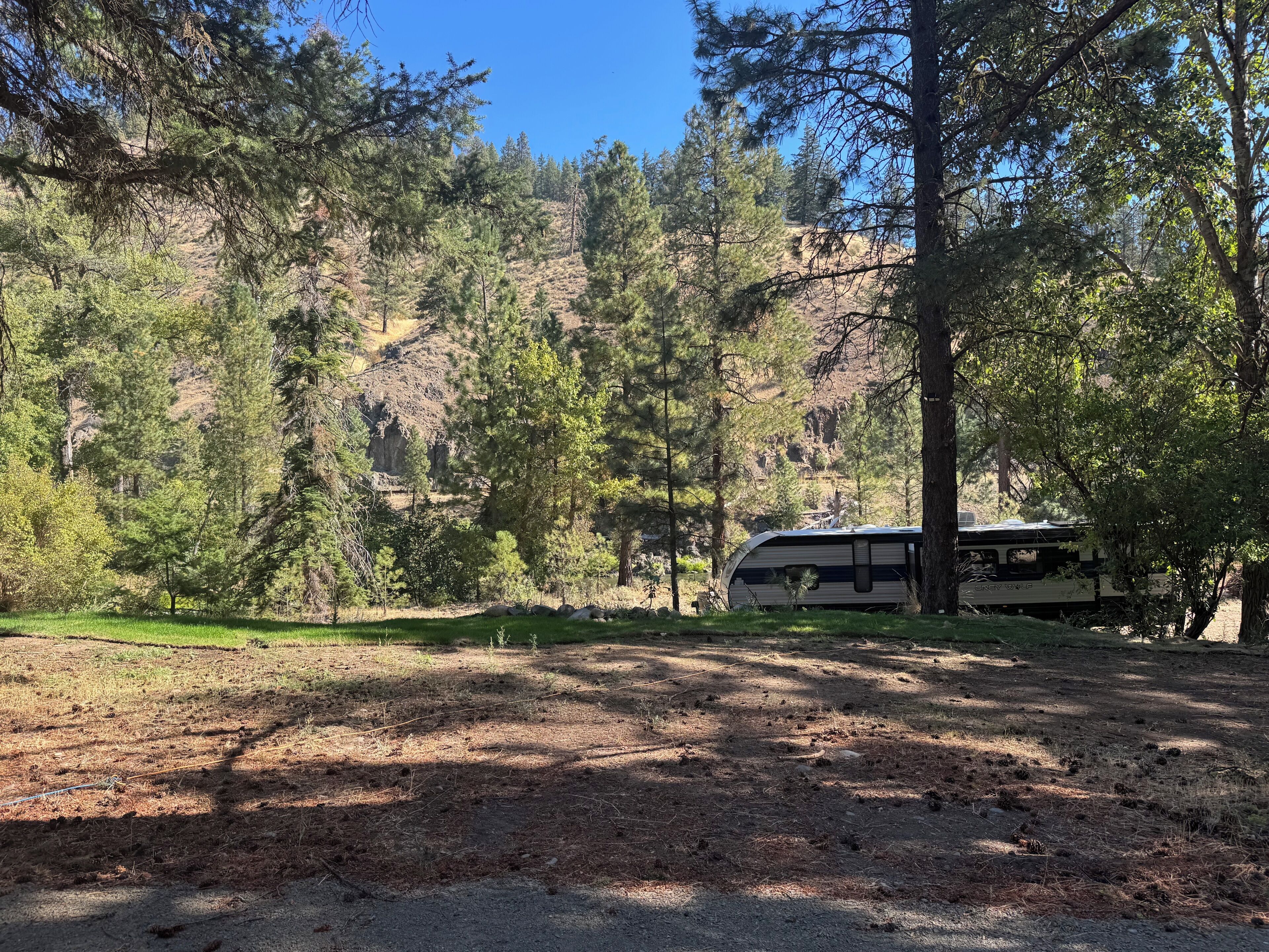 A camping area with a RV parked among trees, a grassy field, and a rocky hillside.