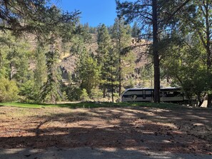 A camping area with a RV parked among trees, a grassy field, and a rocky hillside.