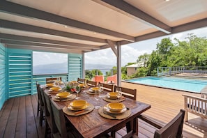 A wooden deck with a table set for dining, overlooking a swimming pool and lush greenery. - Villa Coco Prestige - Three Bedroom Villa, Sleeps 6 (Les Trois-Îlets)