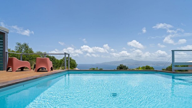 Una piscina con acqua cristallina, circondata da un solarium in legno e due sdraio rosa.