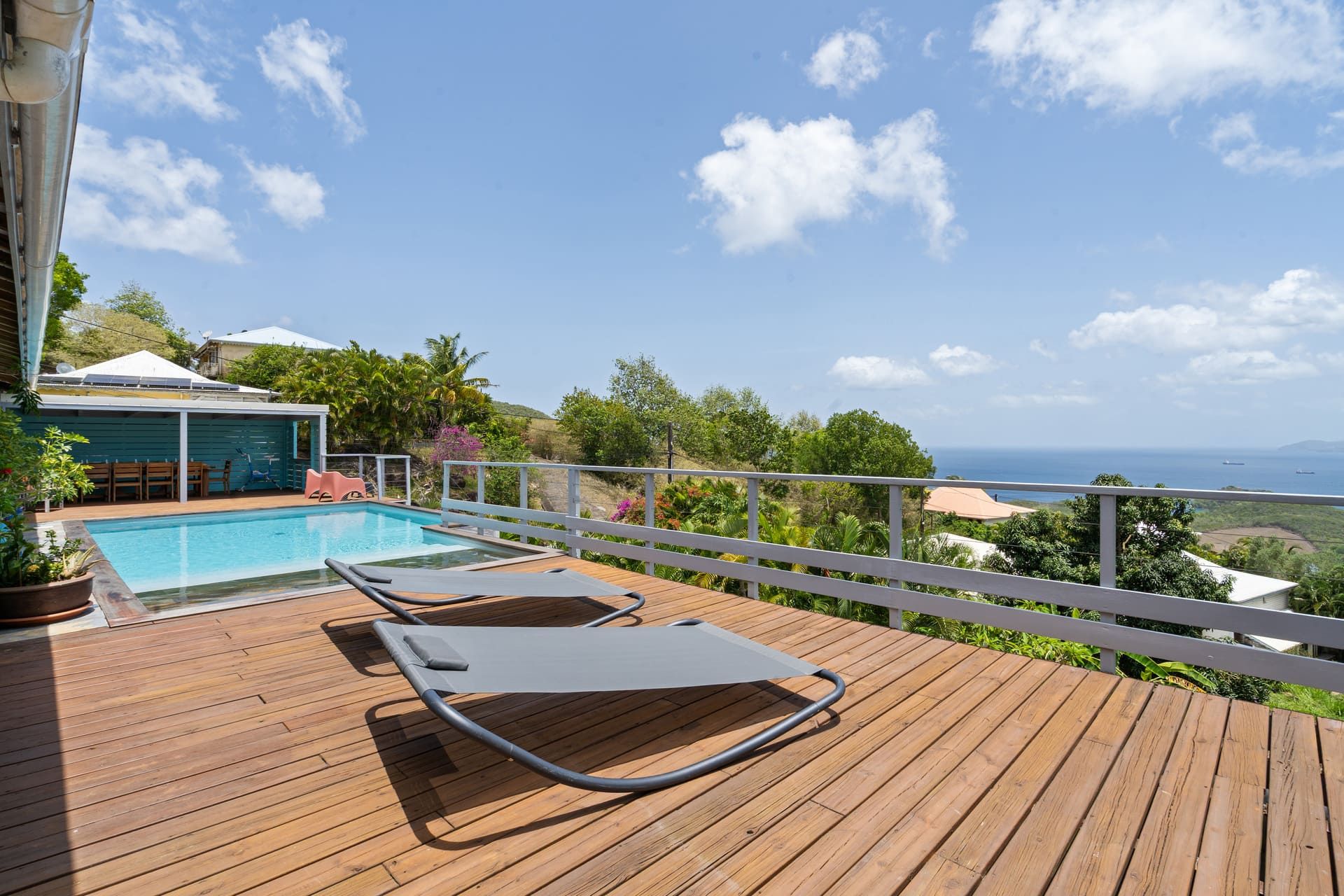 Eine Holzterrasse mit Pool, Liegestühlen und Meerblick.