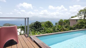 Una piscina con un pontile in legno, una sedia rosa e vista sul mare e sulle montagne.