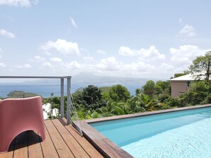 A pool with a wooden deck, a pink chair, and a view of the sea and mountains. - Villa Coco Prestige - Three Bedroom Villa, Sleeps 6 (Les Trois-Îlets)