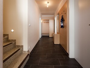 A hallway with a staircase on the left, a wooden door on the right, and a tiled floor. - Holiday Home in Norderney With Wi-fi (Norderney)
