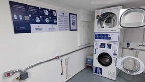 A laundry facility with a large industrial washing machine and a smaller washing machine, both labeled 'LAVA.' - Apartamento GoodLar Liberdade SP  (Liberdade São Paulo)