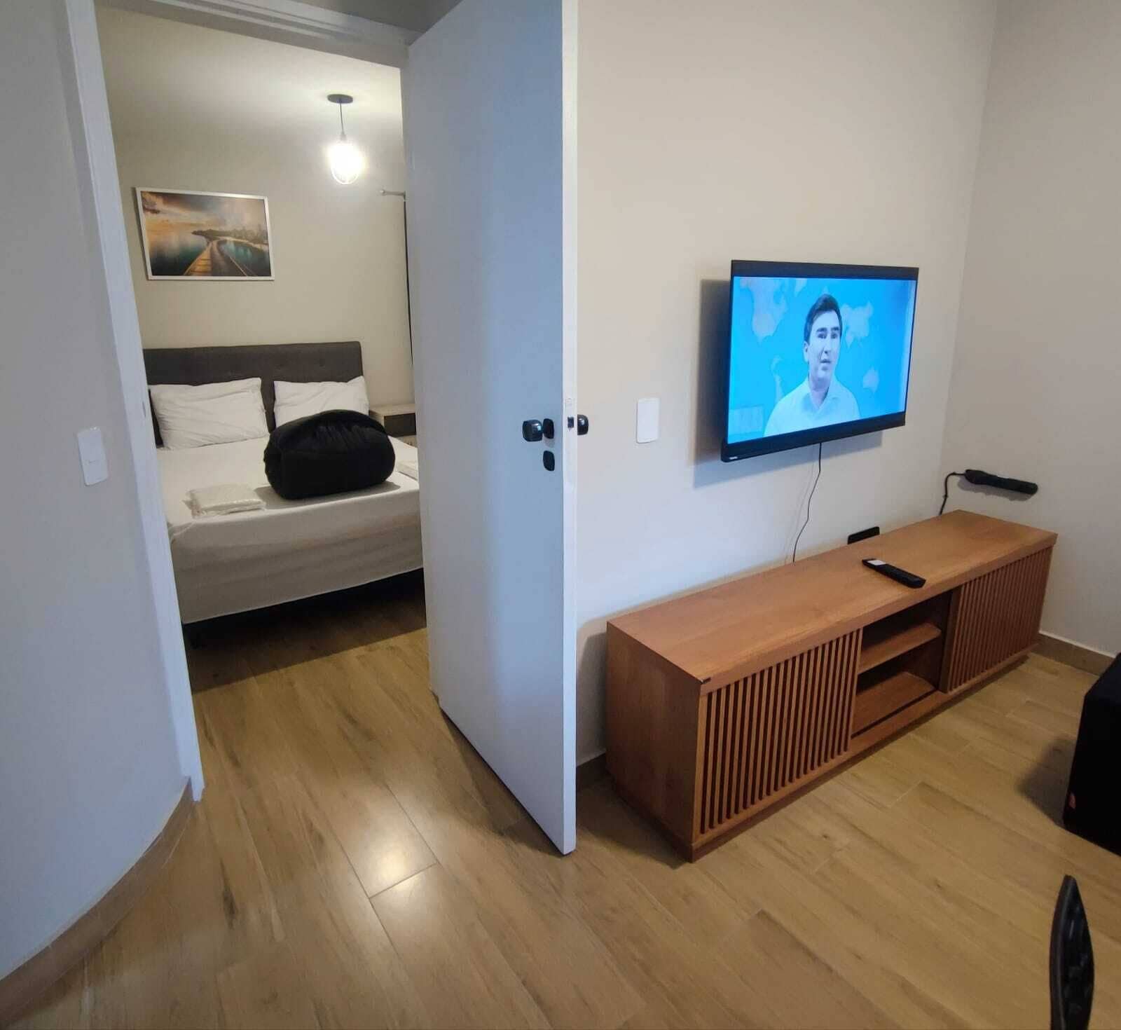 A bedroom with a bed, a TV mounted on the wall, and a wooden console table.