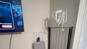 A room with a flat-screen TV mounted on the wall, a radiator, and a small table. - Apartamento GoodLar Liberdade SP  (Liberdade São Paulo)