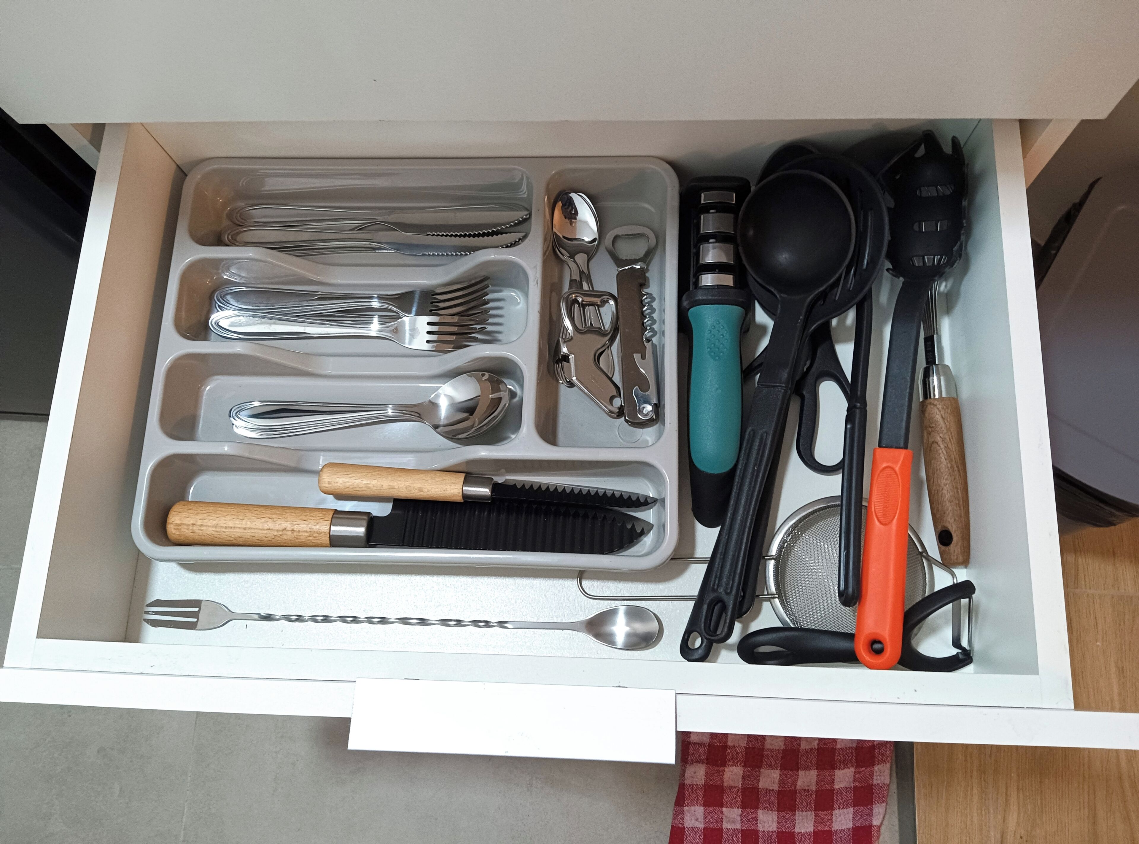 A drawer containing various kitchen utensils including forks, spoons, a knife, and a grater.
