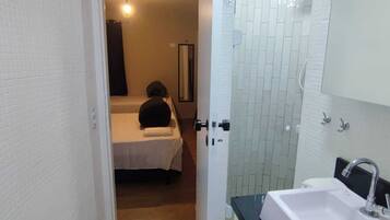 Quarto de hotel com cama, banheiro com pia e espelho, e porta que dá para outro cômodo.
