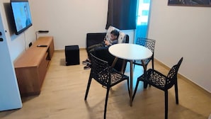 A small, modern room with a round table and four chairs, a television on the wall, a ceiling fan, and a window with curtains. - Apartamento GoodLar Liberdade SP  (Liberdade São Paulo)