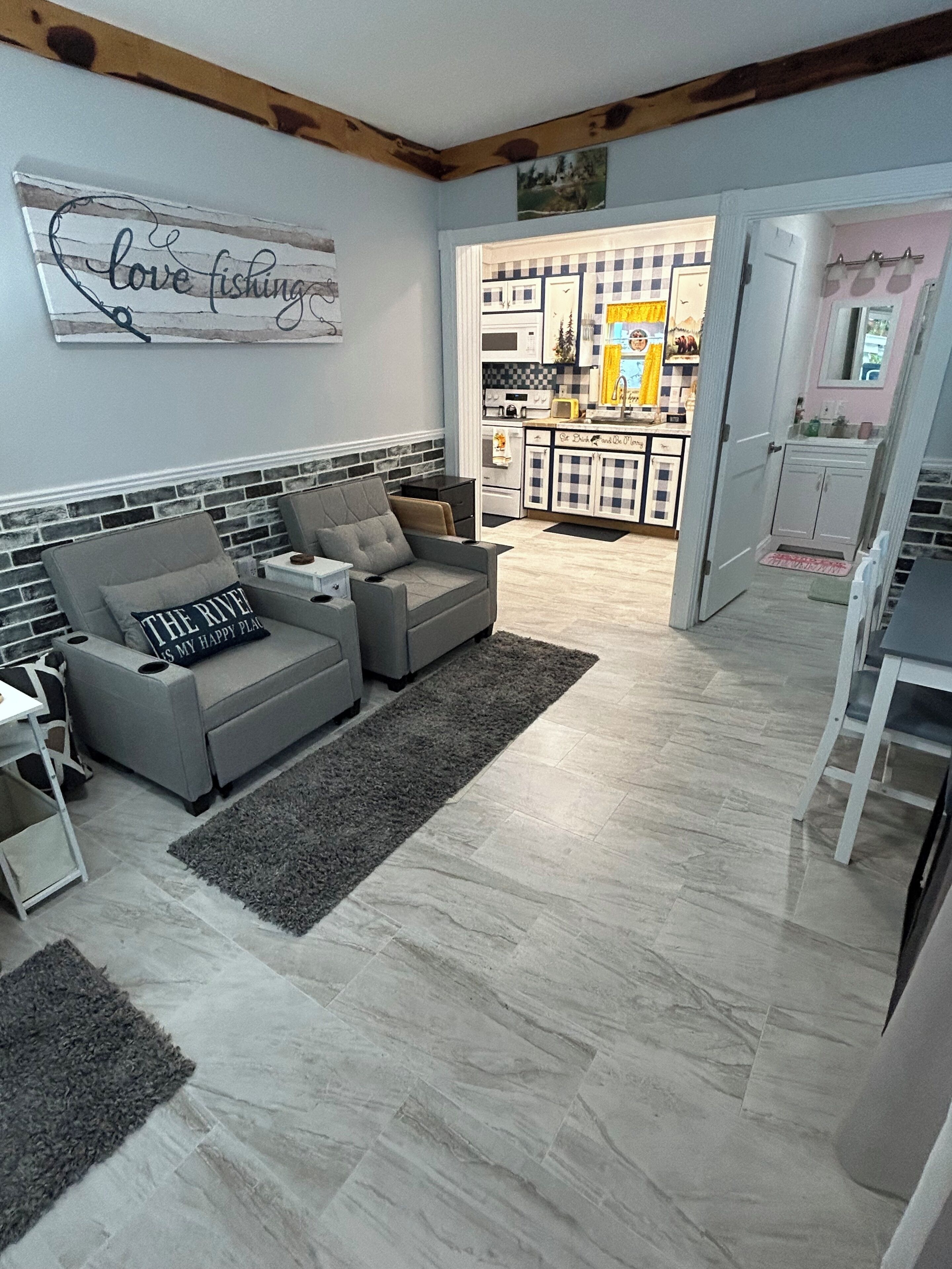 Un salon avec un canapé gris, un tapis et une cuisine en arrière-plan.