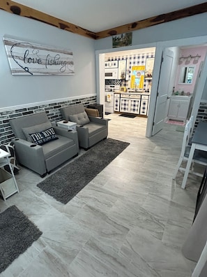 A living room with a grey sofa, a rug, and a kitchen in the background.