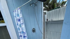 Eine blaue Außenwand mit einer weißen Tür, einem Fenster und einem Duschbereich mit blauer Duschvorhang.