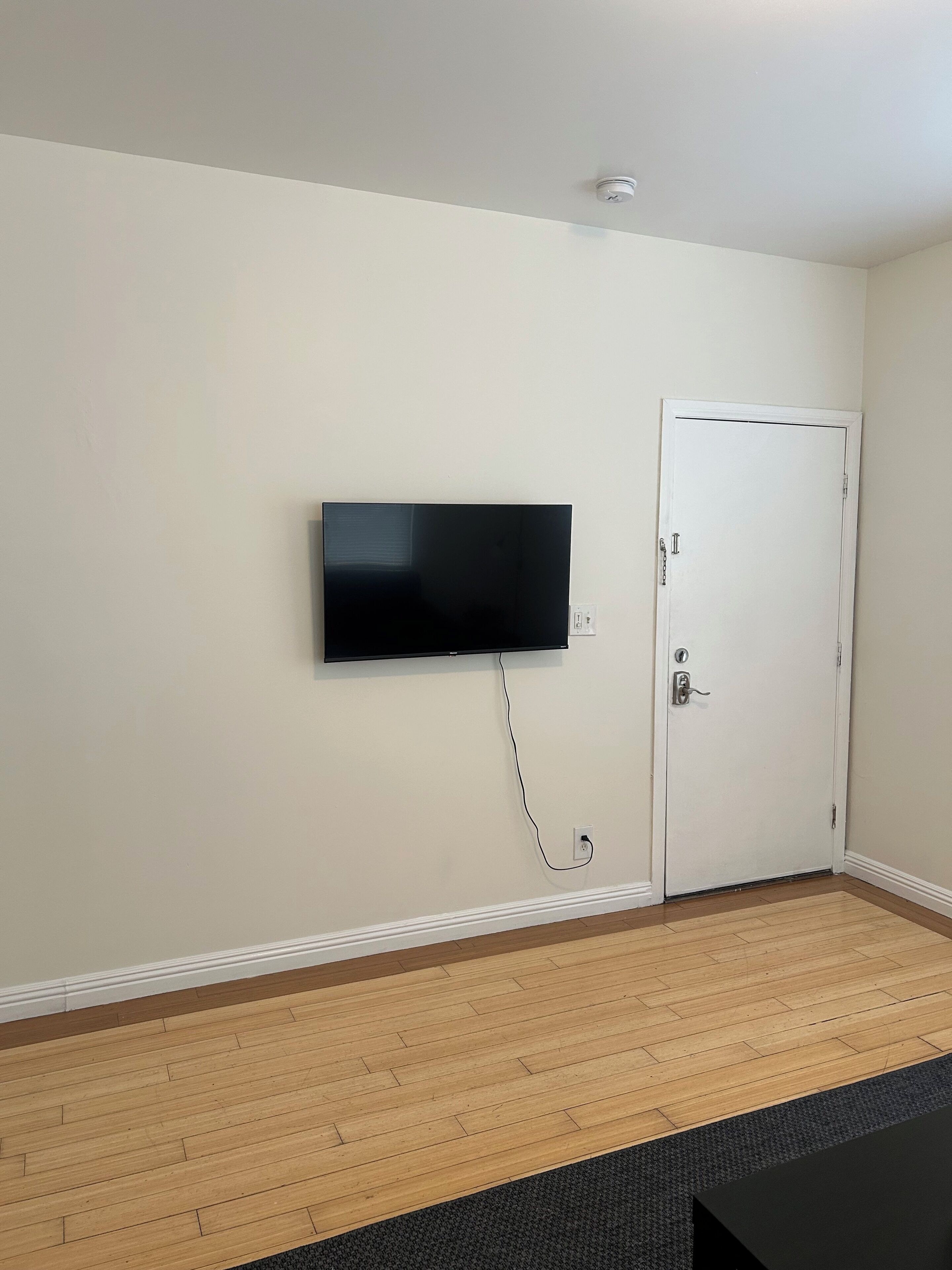 A room with a mounted television, a door, and a wooden floor.