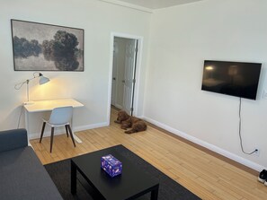 A living room with a desk, a television, a dog, and a coffee table. - A Charming Apartment inDTLA (Los Angeles)