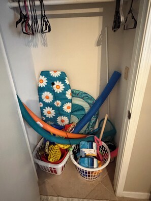 Un espace de rangement avec des paniers contenant des produits de nettoyage et une chaise pliante à motifs floraux.