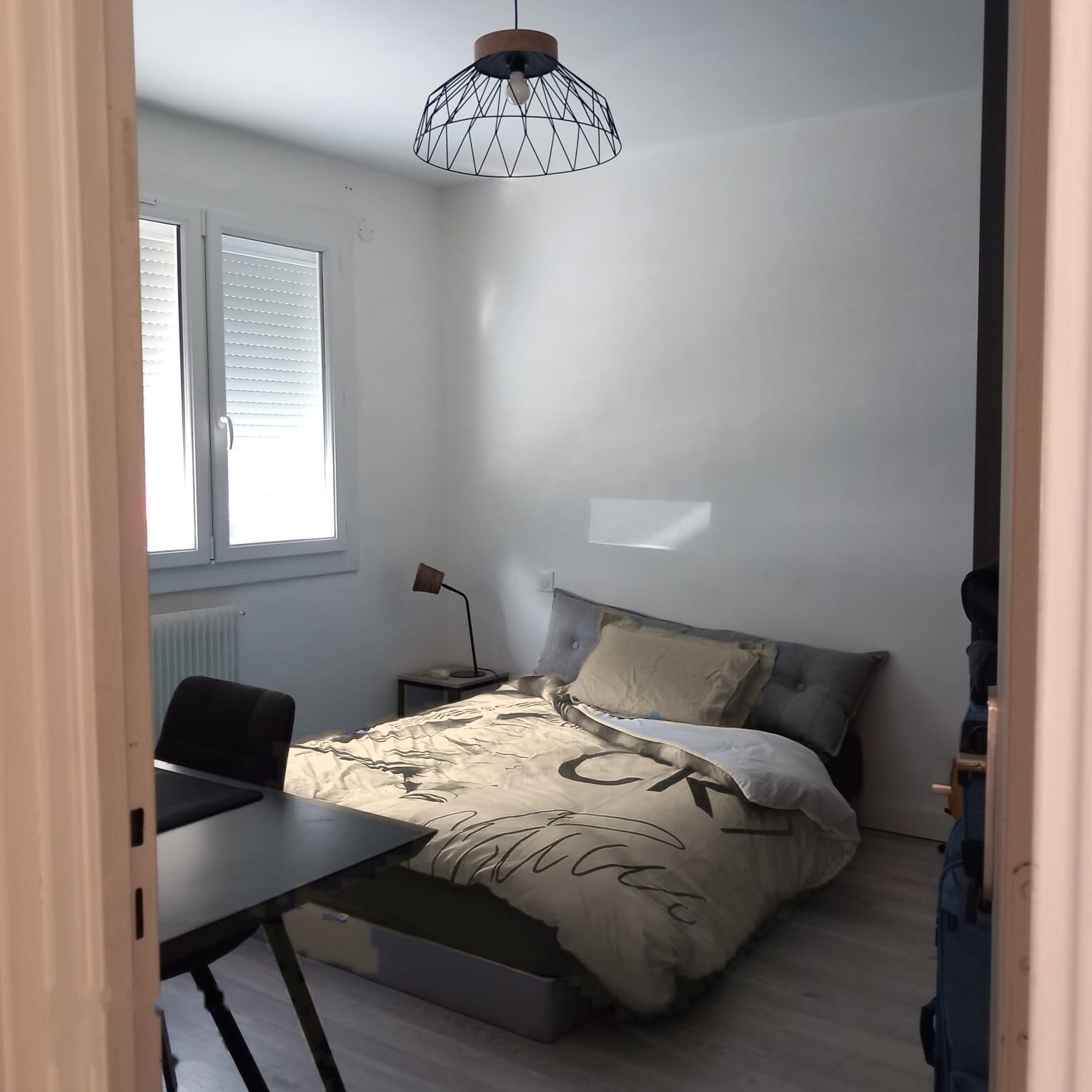 Quarto com cama, escrivaninha, cadeira, abajur e janela.
