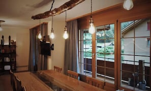 A dining area with a wooden table and chairs, large windows with curtains, and hanging light fixtures. - STUNNING DESIGN APARTMENT IN THE HEART OF LAUTERBRUNNEN (Lauterbrunnen)