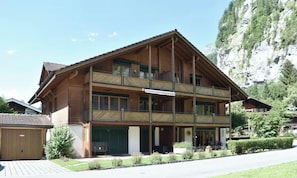 Een houten gebouw met twee verdiepingen, балконы, een garage en een berg op de achtergrond.