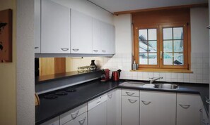 A kitchen with white cabinets, a black countertop, a window with wooden frames, and a stainless steel sink. - STUNNING DESIGN APARTMENT IN THE HEART OF LAUTERBRUNNEN (Lauterbrunnen)